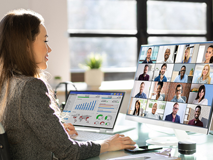 Professional women on a virtual meeting looking a computer screen showing many faces and another screen with charts